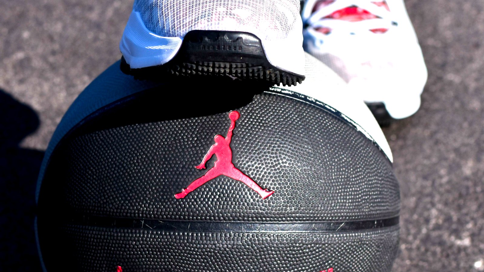 A pair of real Jordans resting on a Jordan basketball on an outdoor court, the Jumpman and the wordmark in red