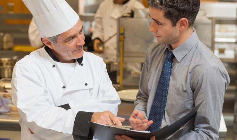 A chef going through paperwork with an inspector in the kitchen