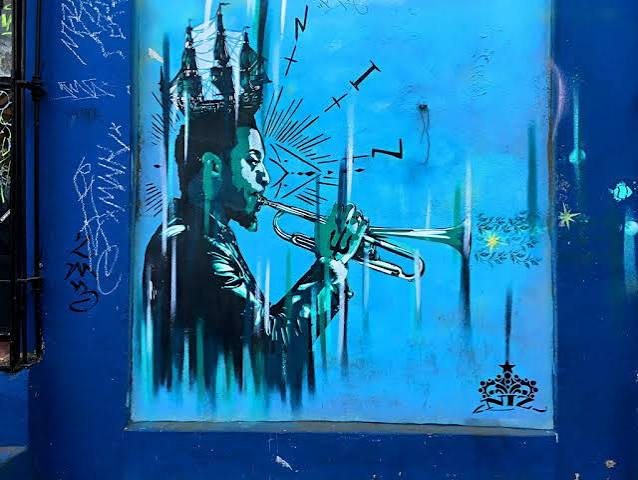 A mural of a trumpet player painted in blues and greens, wearing a crown made of sailing ships