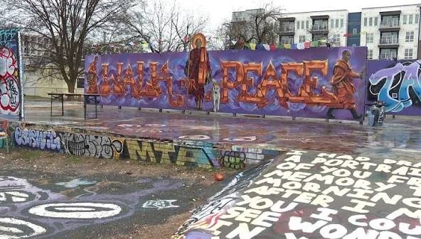 The WALLS OF PEACE wall seen from across a lot covered in spray painted lettering and color